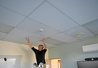 Installing White Acoustic ceiling tiles in an office meeting room.